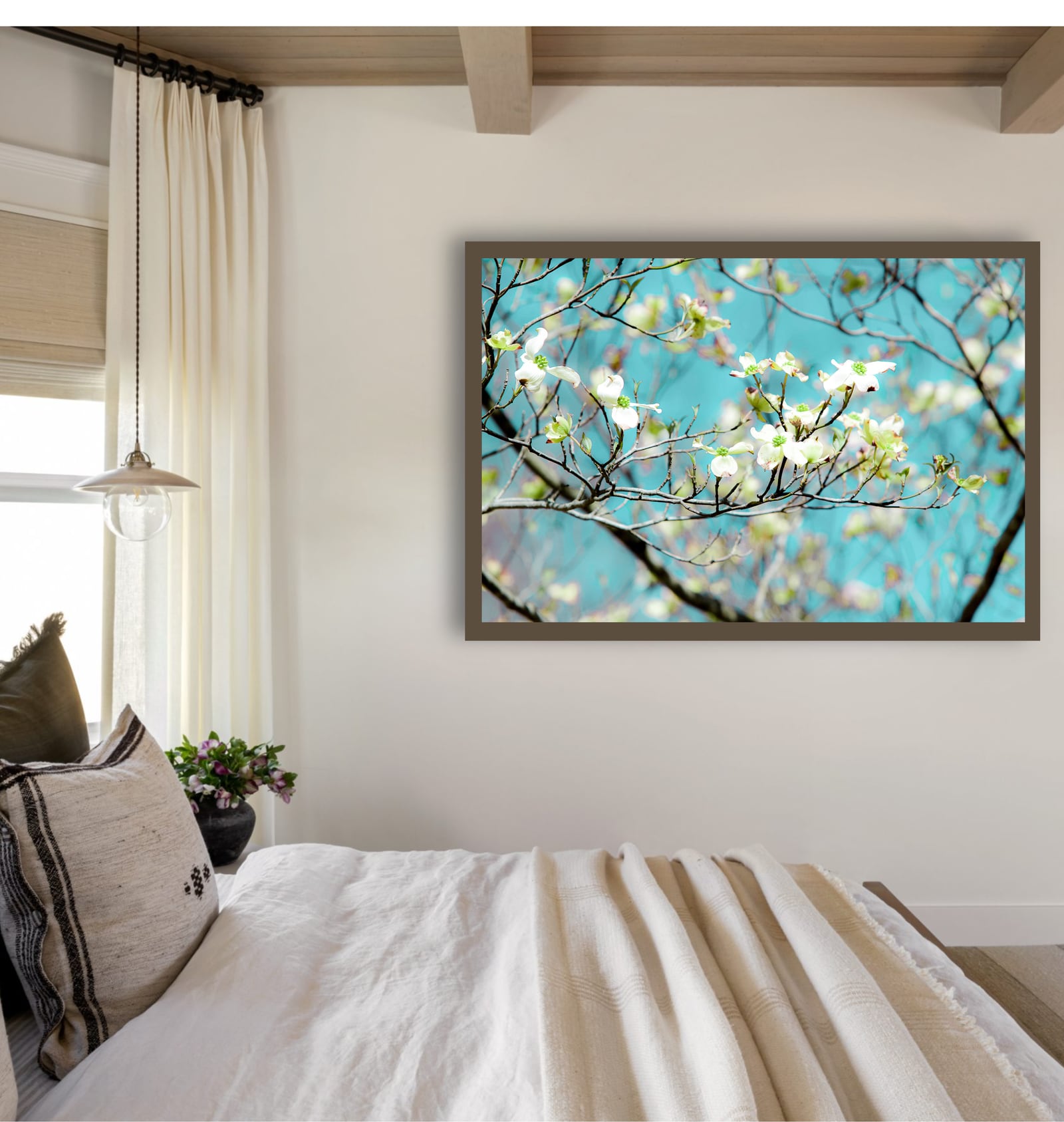 A framed blossom and sky photograph above a bed beside a bright window