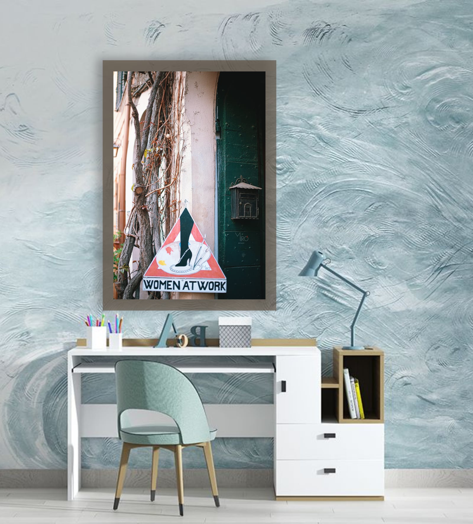 A tall framed street photograph above a desk against a pale blue wall