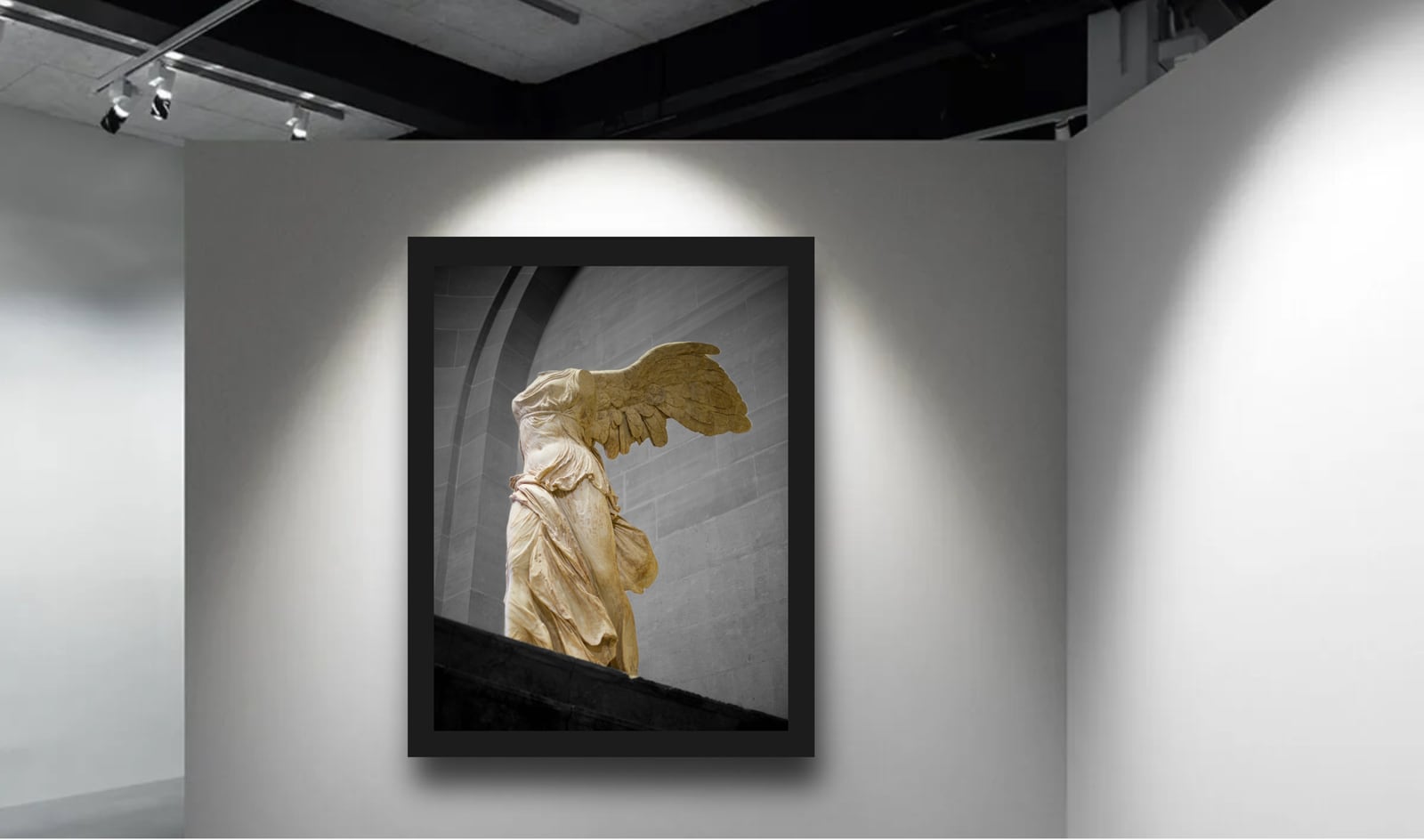 A framed winged sculpture photograph on a dark gallery wall under spotlights